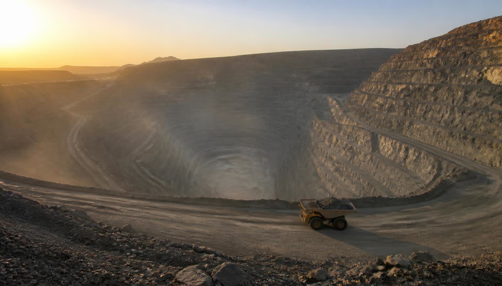 Terraced benches of a vast open-pit gold mine descending toward haul trucks at the pit floor